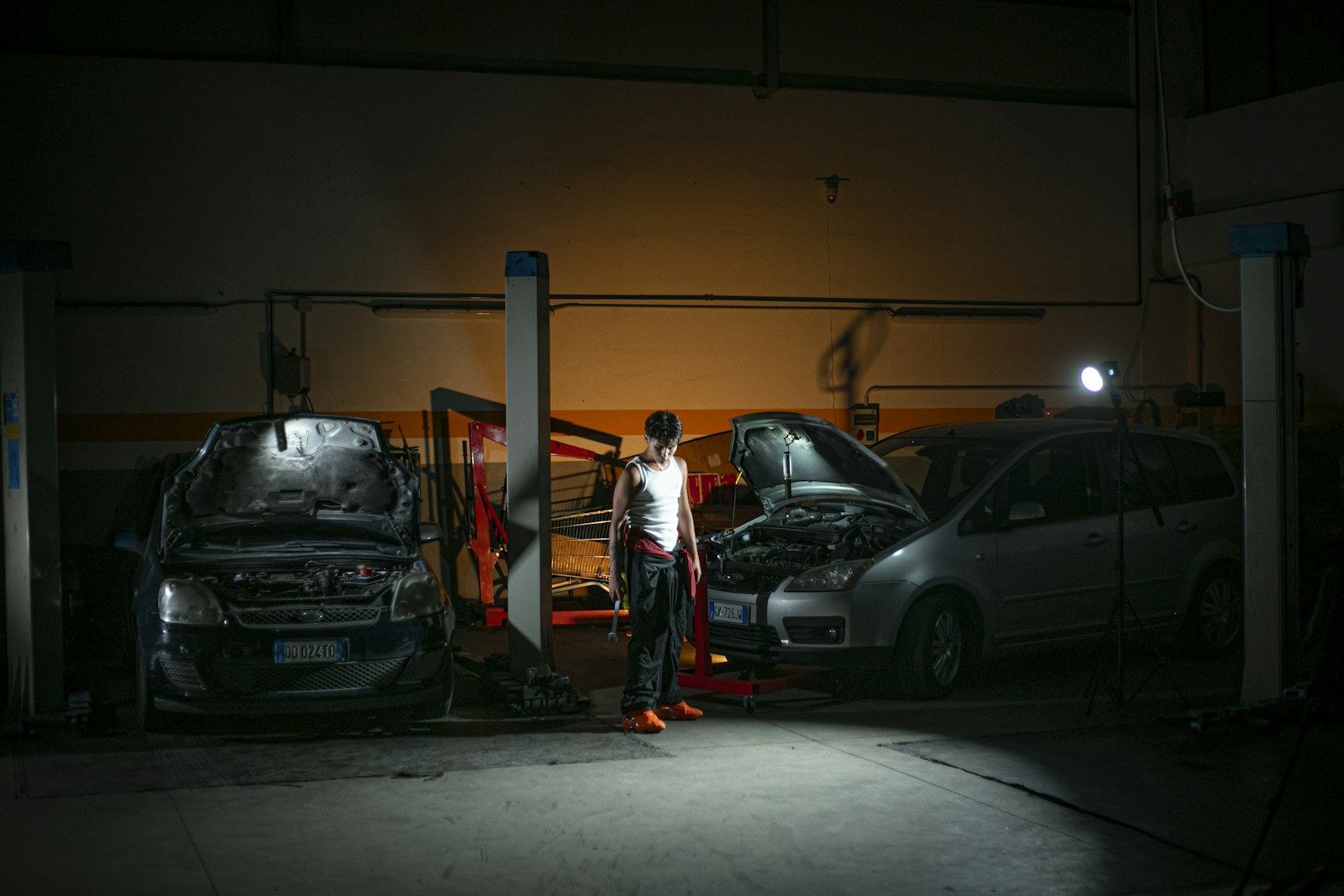 Mechanic working among vehicles in a dimly lit workshop